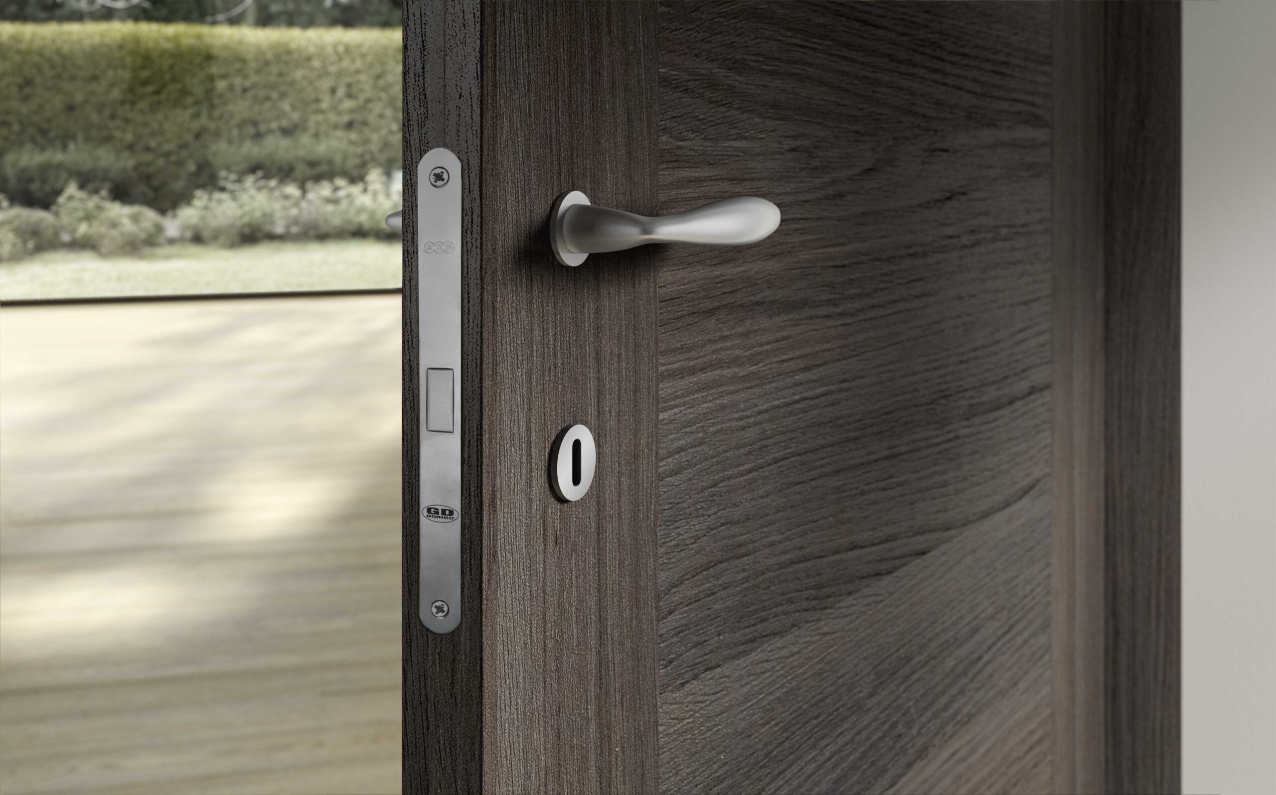 Porta in legno scuro con maniglia moderna in metallo lucido e serratura digitale, vista esterna con giardino sullo sfondo